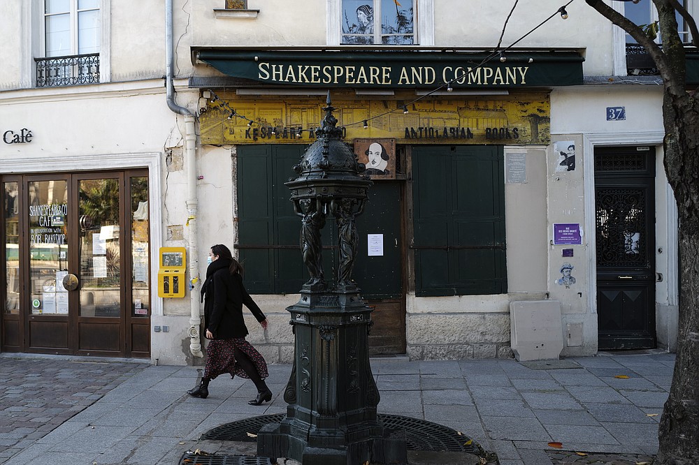 A woman walks by the closed English and American literature Shakespeare and Co. bookstore in Paris, France, Thursday, Nov. 05, 2020. Iconic Parisian bookshop Shakespeare and Co. has launched a support appeal to its readers after its owners say that coronavirus-linked losses, and a crippling months-long lockdown, have left the future of the veritable institution in doubt. "We've been minus 80 percent since the first confinement in March, so at this point we've used all our savings," Sylvia Whitman, daughter of the shop's co-founder George Whitman, told the Associated Press. (AP Photo/Francois Mori)