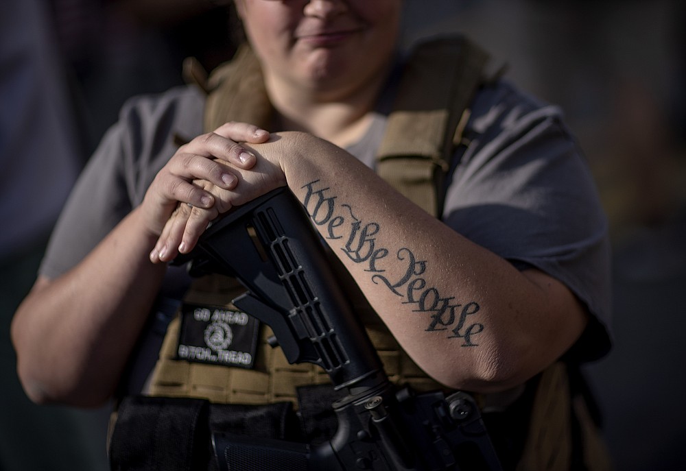 The tattoo "We The People", a phrase from the United States Constitution, decorates the arm of Trump supporter Michelle Gregoire as she rests her hand on her gun during a protest over the election results outside the central counting board at the TFC Center in Detroit, Friday, Nov. 6, 2020. (AP Photo/David Goldman)