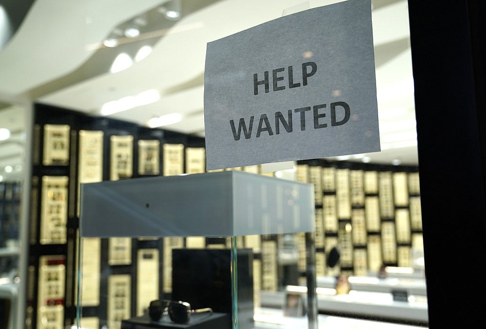 A Help Wanted sign is posted at a Designer Eyes store at Brickell City Centre, Friday, Nov. 6, 2020, in Miami. Defying fears of another slowdown, U.S. businesses kept hiring at a solid pace in October yet there are signs they remain cautious about the economy's future as the pandemic worsens. (AP Photo/Lynne Sladky)