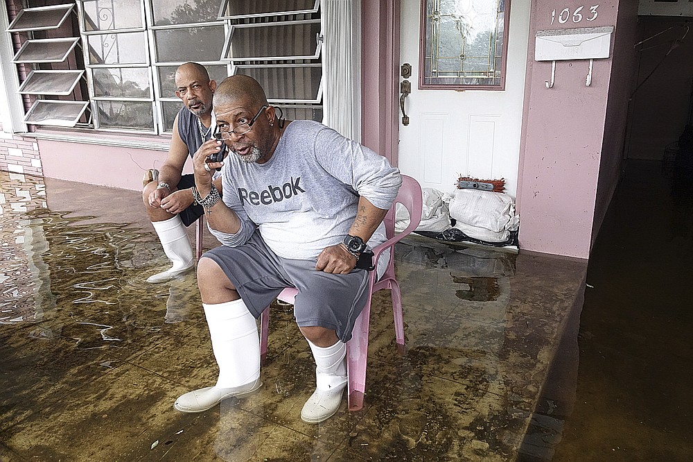 Dalvin, left, and his brother Eric Gaines sit on the porch of thier flooded home in Melrose Park in Fort Lauderdale, Fla., Tuesday, Nov. 10, 2020. Tropical Storm Eta is squatting off western Cuba, and forecasters say it's unclear where it might strike land again. It dumped torrential rain on Cuba and South Florida, flooding entire neighborhoods. (Joe Cavaretta/South Florida Sun-Sentinel via AP)