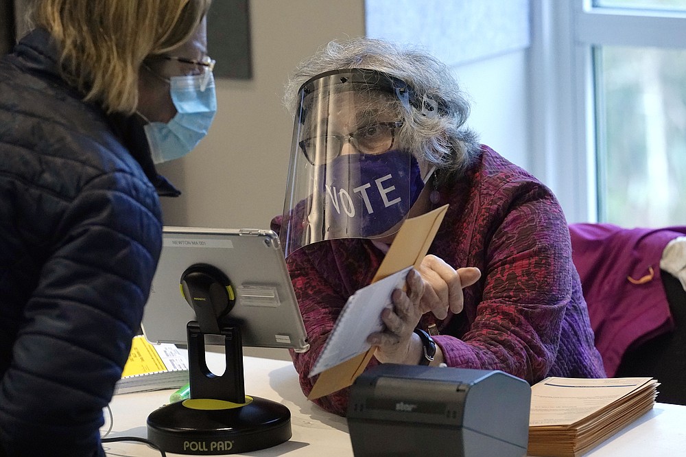 FILE - In this Oct. 28, 2020, file photo, poll worker Alice Machinist, of Newton, Mass., right, wears a mask and shield out of concern for the coronavirus while assisting a voter, left, with a ballot during early in-person general election voting at the Newton Free Library, in Newton, Mass. The 2020 presidential election had all the makings of a looming disaster: fears of Russian meddling, violence at the polls, voter intimidation and poll workers fleeing their posts over the coronavirus. But the election was largely smooth, in large part because 107 million voters that cast their ballots early and took the pressure off Election Day operations. (AP Photo/Steven Senne, File)