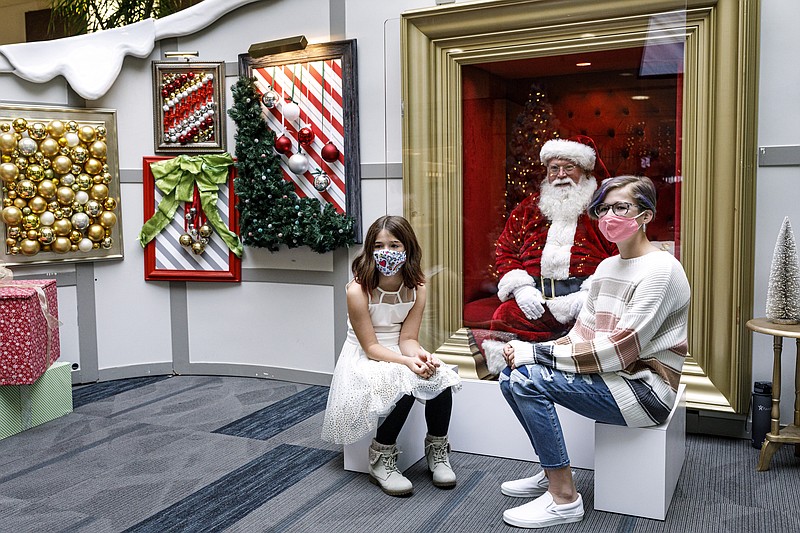 Sisters Harper, left, and Emmersyn Houck, of Duncannon, Pa., visits with Santa Claus, with safety protocols in place, at Capital City Mall in Lower Allen Township,  Pa., on Wednesday, Nov. 11, 2020.  Malls are doing all they can to keep the jolly old man safe from the coronavirus, including banning kids from sitting on his knee, completely changing what a Santa visit looks like. (Dan Gleiter/The Patriot-News via AP)