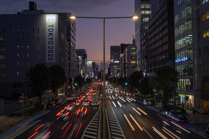 FILE - This Oct. 12, 2020, file photo shows the streaks of lights from the cars passing by a Tokyo 2020 Olympics and Paralympics sign on the side of a building, in Tokyo, as the sky is colored by the sunset. Japan's economy grew at an annual rate of 21.4% in the last quarter in a recovery from the shocks of the pandemic driven by both private spending and exports. (AP Photo/Kiichiro Sato, File)