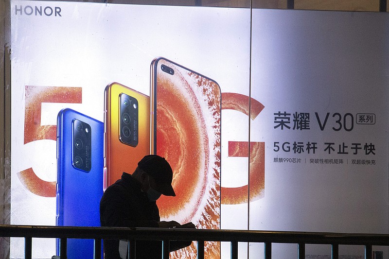 A man stands near an advertisement for Huawei's Honor brand 5G phones in Beijing on Thursday, Feb. 27, 2020. In an announcement Tuesday, Nov. 17, 2020, Chinese tech giant Huawei says it is selling its budget-price Honor smartphone brand in an effort to rescue the struggling business from damaging U.S. sanctions imposed on its parent company. (AP Photo/Ng Han Guan)