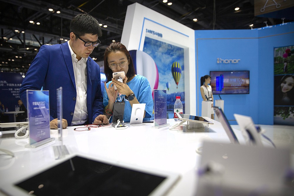 A staff member talks to a visitor at a booth for Chinese smartphone brand Honor at the Global Mobile Internet Conference in Beijing on April 26, 2018. In an announcement Tuesday, Nov. 17, 2020, Chinese tech giant Huawei says it is selling its budget-price Honor smartphone brand in an effort to rescue the struggling business from damaging U.S. sanctions imposed on its parent company. (AP Photo/Mark Schiefelbein)