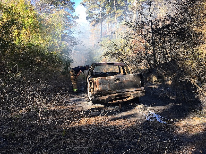 A Hot Springs firefighter examines a burned-out pickup truck that was discovered at the scene of a small forest fire Thursday. - Photo by Richard Rasmussen of The Sentinel-Record