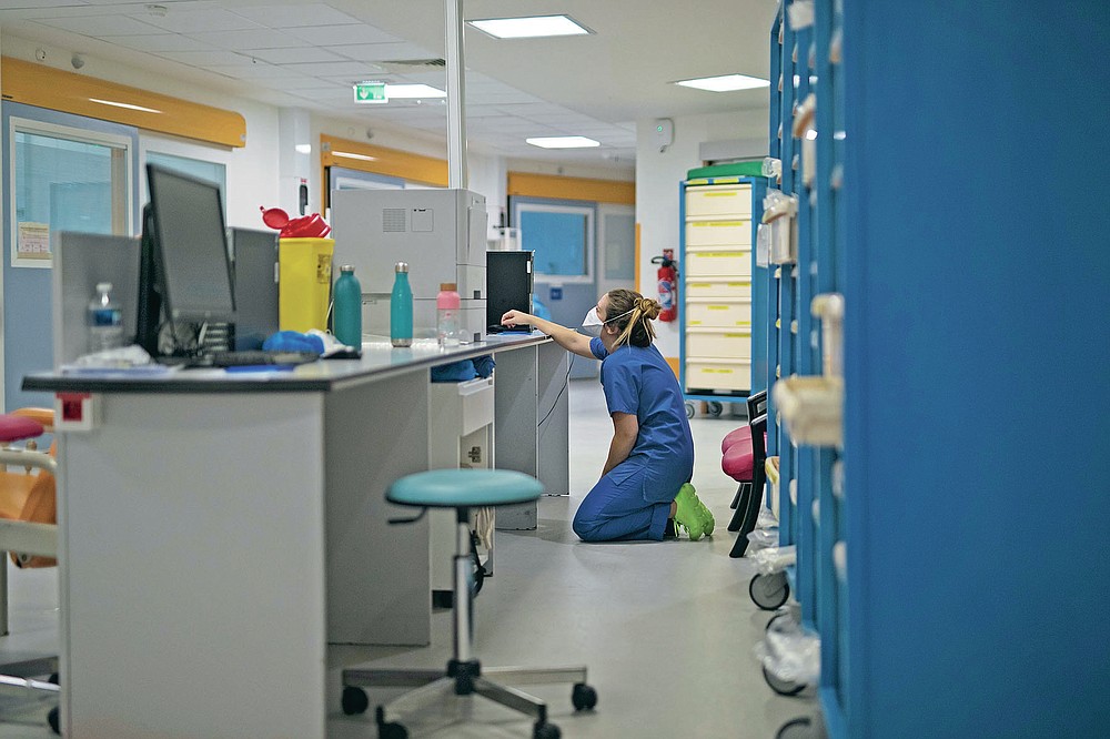 A nurse rests her knees on the floor as she looks at a computer screen during the day shift at the COVID-19 ICU of the La Timone hospital in Marseille, southern France, Thursday, Nov. 12, 2020. (AP Photo/Daniel Cole)