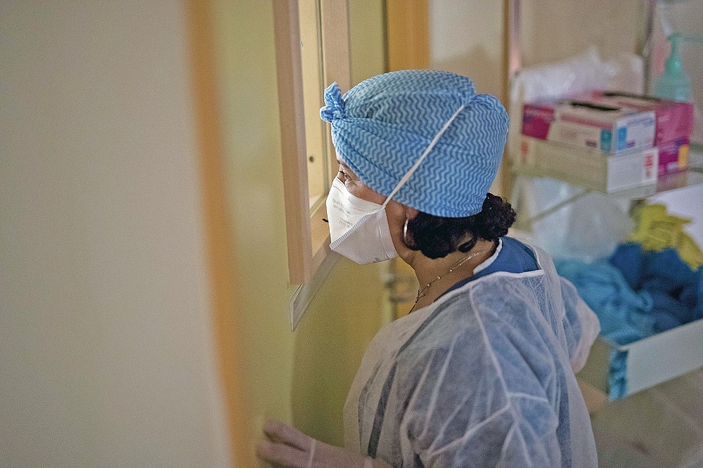 A night shift nurse watches through the window of a makeshift ICU room as nurses install a newly admitted COVID-19 patient whose worsening condition forced doctors to fill the last available COVID-19 ICU bed that night at the La Timone hospital in Marseille, southern France, Friday, Nov. 13, 2020. (AP Photo/Daniel Cole)