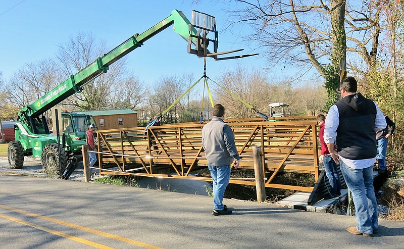 Westside Eagle Observer/SUSAN HOLLAND
Gravette mayor Kurt Maddox (center) and city building inspector/code enforcement officer David Keck (right) look on as crane operator Rome Wesson lowers the bridge into place on the walking trail on 2nd Avenue S.W. The bridge was installed on Tuesday morning, Nov. 17, by workmen from 81 Construction Group of Siloam Springs.