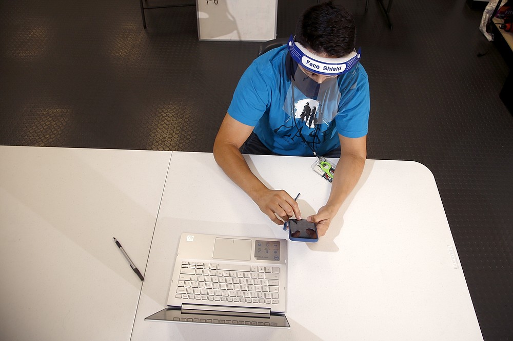 FILE - In this Aug. 6, 2020, file photo wearing a face covering and face shield while working due to the coronavirus, Maico Olivares, lead voter registration organizer for Central Arizonans for a Sustainable Economy, works his phone and computer as he tries to reach about 25 people a day, mostly within the Latino community, to persuade them to register to vote in Phoenix. (AP Photo/Ross D. Franklin, File)
