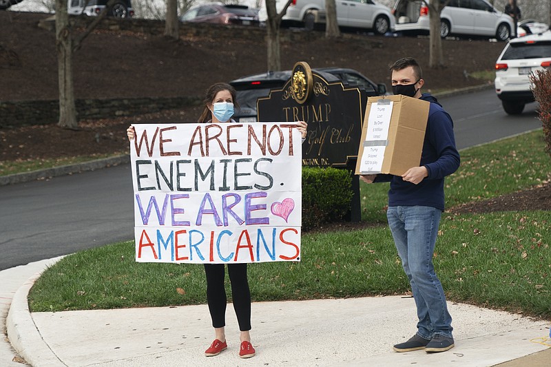 As the motorcade carrying President Donald Trump arrives at Trump National Golf Club, Sunday, Nov. 22, 2020, in Sterling, Va., people hold up signs. (AP Photo/Jacquelyn Martin)