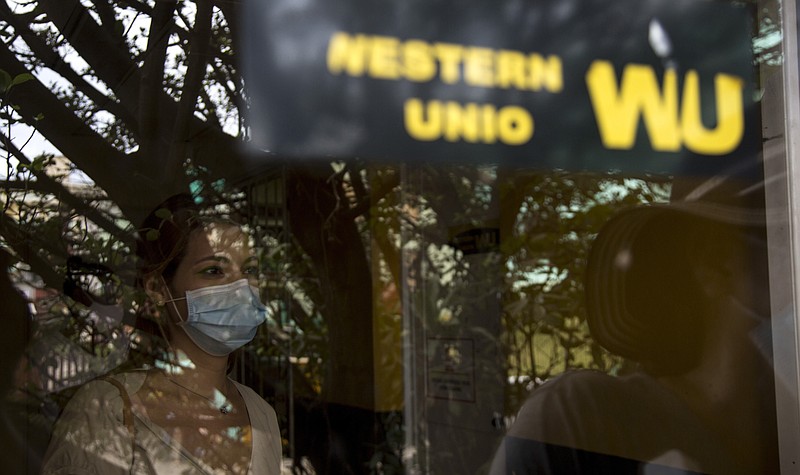 Photographed through a window, a woman waits to collect money at a Western Union office on its last day of business in Havana, Cuba, Monday, Nov. 23, 2020. Restrictions from the Trump administration on the military-controlled operator that handles cash deposits will go into effect Monday at 6 p.m. local, keeping Cubans from being able to retrieve money sent from abroad through Western Union – the main source of cash remittances for many families. (AP Photo/Ismael Francisco)