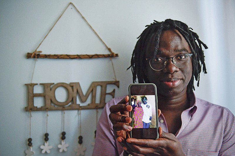 Mbaye Babacar Diouf, 33, displays a photo of himself with his Senegal's mother on a phone, in his house in the basque city of Algorta, northern Spain, Wednesday, Nov. 18, 2020. Mbaye Babacar Diouf's life as a migrant in Europe took a turn for the better when he was adopted in Spain at the age of 28. That enabled him to pay his debts to human traffickers, study nursing and find a job at a Spanish hospital. Now he's giving back to the community. In a Bilbao hospital he cares for COVID-19 patients.  (AP Photo/Alvaro Barrientos)