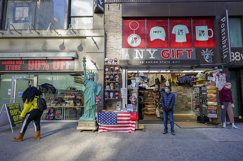 A shop keeper at a gift shop along 34th Street stands on the sidewalk waiting for customers, Friday, Nov. 20, 2020, in New York. In souvenir shops from Times Square to the World Trade Center, shelves full of T-shirts and trinkets still love New York, as the slogan goes. But the proprietors wonder when their customers will, again. The coronavirus has altered many aspects of life and business in the United States' biggest city, and the pandemic is taking a major toll on the gifts-and-luggage stores that dot tourist-friendly areas. After setting records year after year since 2010, travel to New York has plummeted during the pandemic. (AP Photo/Mary Altaffer)