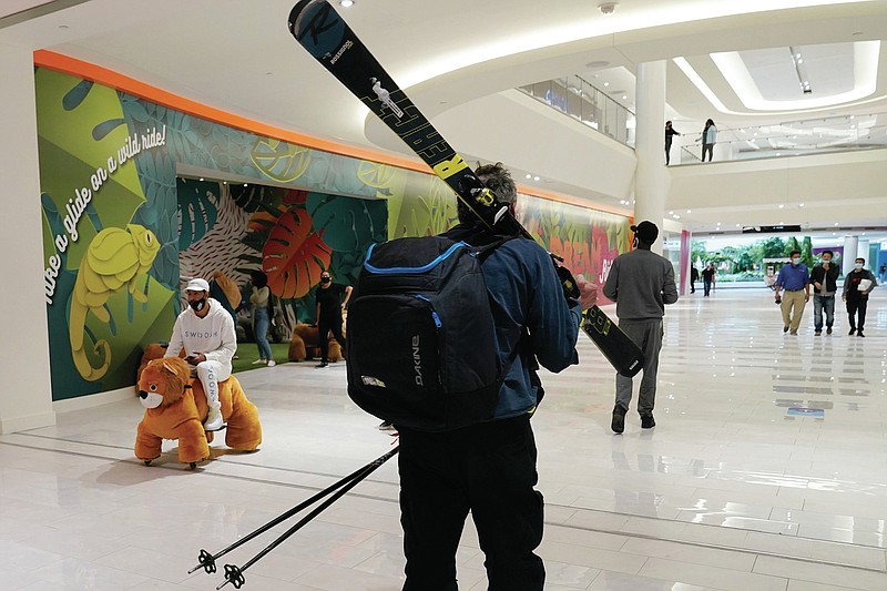 A man carries a set of skis and ski poles as he walks through the American Dream Mall after visiting "The Big Snow," a ski slope inside the giant mall, Thursday, Oct. 1, 2020, in East Rutherford, New Jersey. The mall reopened Thursday after it abruptly closed down in March due to concerns over the spread of coronavirus. (AP Photo/Kathy Willens)