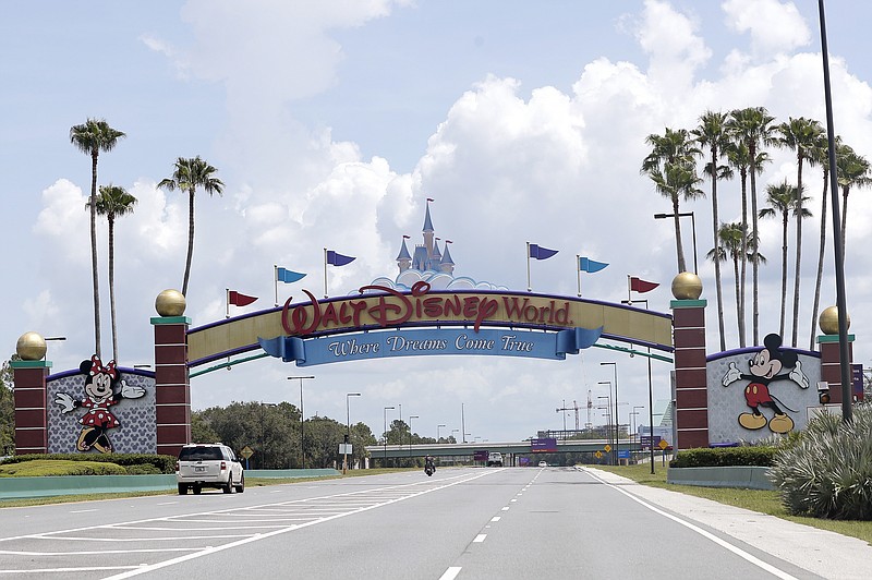 FILE - In this Thursday, July 2, 2020, file photo, cars drive under a sign greeting visitors near the entrance to Walt Disney World, in Lake Buena Vista, Fla.   The Walt Disney Co. is announcing plans to lay off 4,000 more workers in its theme parks division in California and Florida due to the COVID-19 pandemic's effect on the industry. The company has been limiting attendance at its parks and changing protocols to allow for social distancing. (AP Photo/John Raoux, File)