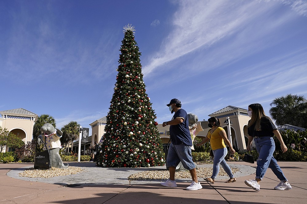 Shoppers wear protective face masks as they walk past a Christmas setting at the Ellenton Premium Outlet stores Friday, Nov. 27, 2020, in Ellenton, Fla. Attendance at the mall was down in an attempt to avoid spreading the corona virus. (AP Photo/Chris O'Meara)