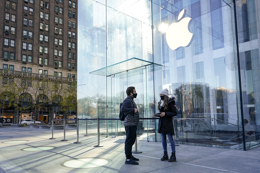 An Apple Store associate, right, wears a face mask as she helps a Black Friday shopper outside their store along Fifth Avenue, Friday, Nov. 27, 2020, in New York. (AP Photo/Mary Altaffer)