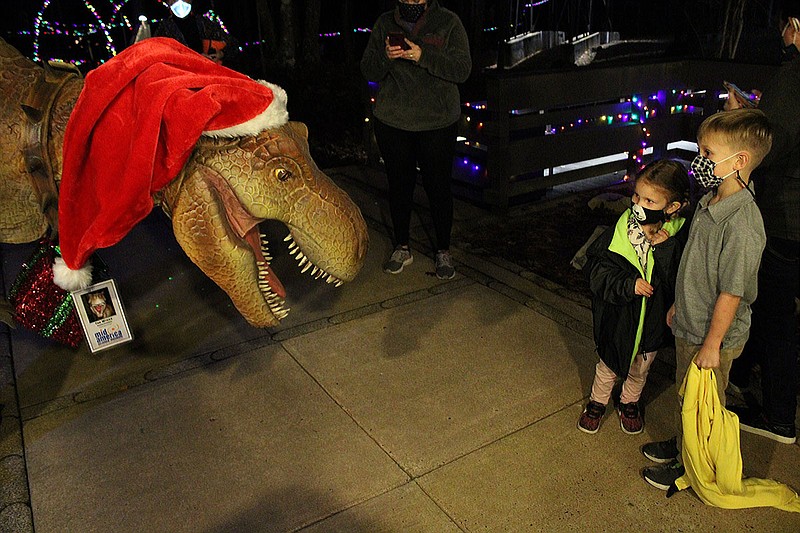 Tee Wrexx, a walk-around dinosaur at Mid-America Science Museum, greets two young visitors to the museum Friday on the opening night of Dino-Lites. - Photo by Tanner Newton of The Sentinel-Record