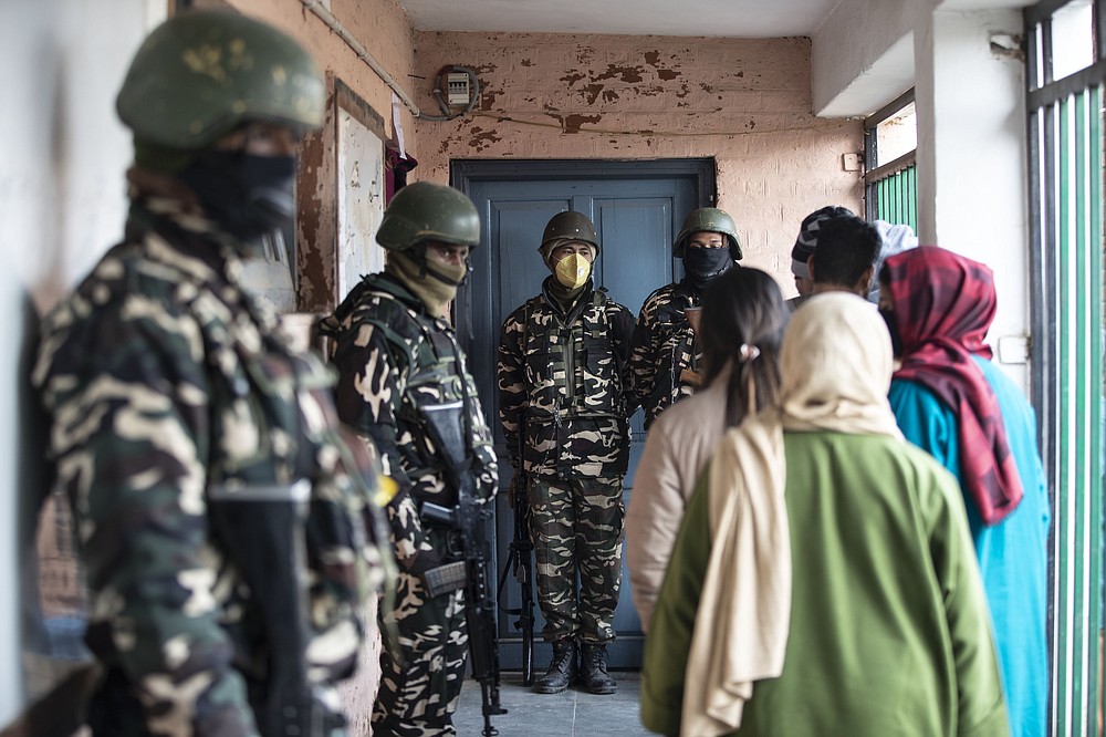 Soldiers stand guard as Kashmiris wait outside a polling booth to cast their votes during the first phase of District Development Councils election on the outskirts of Srinagar, Indian controlled Kashmir, Saturday, Nov. 28, 2020. Thousands of people in Indian-controlled Kashmir voted Saturday amid tight security and freezing cold temperatures in the first phase of local elections, the first since New Delhi revoked the disputed region's semiautonomous status. (AP Photo/Mukhtar Khan)