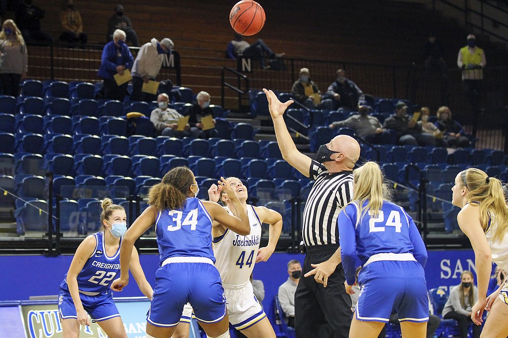 This photo provided by South Dakota State Athletics shows Creighton and South Dakota State women's college basketball players during a jump ball in an NCAA college basketball game in Brookings, South Dakota, Monday, Nov. 30, 3030. From left are Creighton's Carly Bachelor (22), Creighton's Mykel Parham (34) South Dakota State's Myah Selland (44) and Creighton's Chloe Dworak (34). It's a common sight to see players and coaches wear masks on the sideline so far this season during college basketball games to help prevent the spread of the coronavirus. The DePaul and Creighton women's basketball teams are among a few squads that have taken it a step further with their players wearing the masks while they are on the court playing.(Christian Gravius/South Dakota State Athletics via AP)