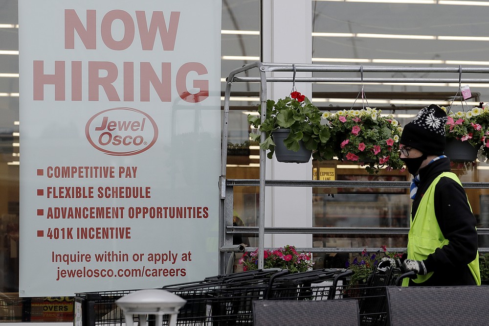 A man pushes carts as a hiring sign shows at a Jewel Osco grocery store in Deerfield, Ill., Thursday, April 23, 2020. Friday, Dec. 4,  monthly U.S. jobs report will help answer a key question hanging over the economy: Just how much damage is being caused by the resurgent coronavirus, the resulting restrictions on businesses and the reluctance of consumers to shop, travel and dine out? (AP Photo/Nam Y. Huh)