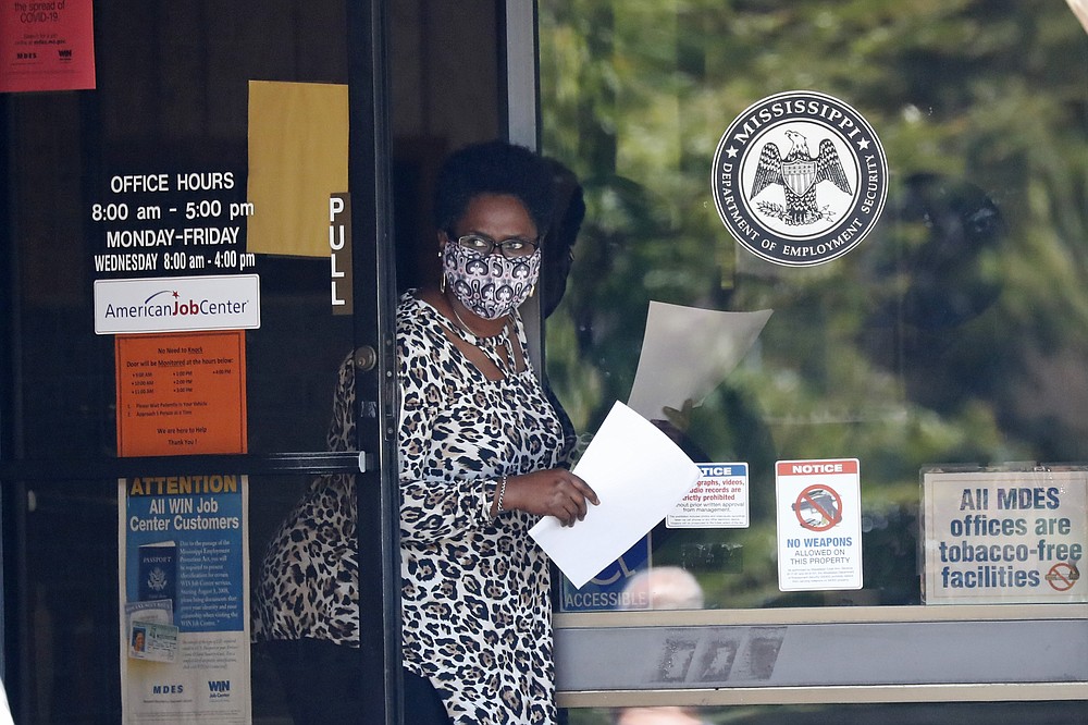 FILE - In this April 21, 2020 file photo, a worker wearing a mask to protect against coronavirus, holds an unemployment benefit application form as she waits for a client at the state WIN job center in Pearl, Miss.  Friday, Dec. 4,  monthly U.S. jobs report will help answer a key question hanging over the economy: Just how much damage is being caused by the resurgent coronavirus, the resulting restrictions on businesses and the reluctance of consumers to shop, travel and dine out?  (AP Photo/Rogelio V. Solis, File)