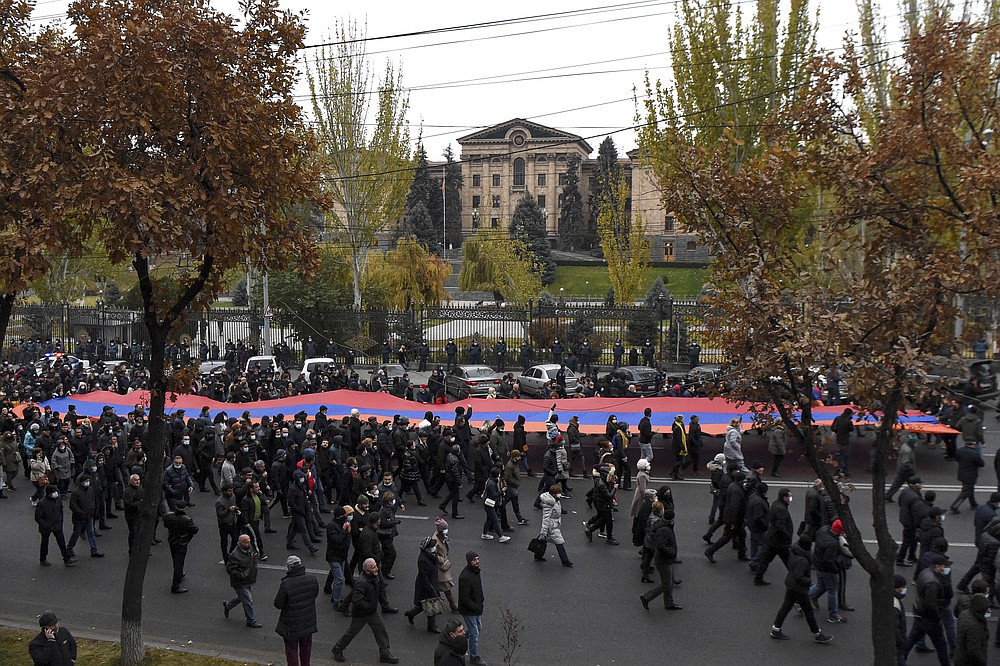 Opposition demonstrators carry a giant an Armenian national flag as they rally to pressure Armenian Prime Minister Nikol Pashinyan to resign over a peace deal with neighboring Azerbaijan in Republic Square in Yerevan, Armenia, Saturday, Dec. 5, 2020. Tens of thousands of opposition supporters marched across the Armenian capital Saturday to push for the resignation of the ex-Soviet nation's prime minister over his handling of the conflict with Azerbaijan over Nagorno-Karabakh. (Lusi Sargsyan/PHOTOLURE via AP)