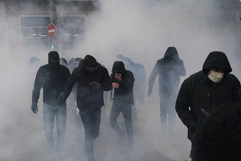 Protesters walk through the tear gas during a demonstration in Lyon, central France, Saturday, Dec. 5, 2020. Thousands marched in protests around France on Saturday against a contested security bill with tensions quickly rising at the Paris march as intruders set fire to several cars, broke windows and tossed objects at police. (AP Photo/Laurent Cipriani)