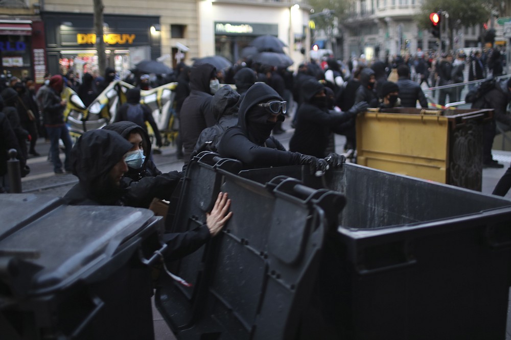 Youths pull garbage bins during a demonstration Saturday, Dec. 5, 2020 in Marseille, southern France. Thousands marched in protests around France on Saturday against a contested security bill with tensions quickly rising at the Paris march as intruders set fire to several cars, broke windows and tossed projectiles at police. (AP Photo/Daniel Cole)