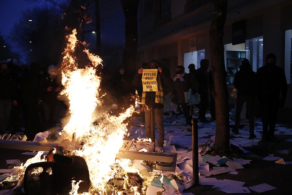 A man holds a poster reading "Living yes, surviving no" during a demonstration Saturday, Dec. 5, 2020 in Paris. Thousands marched in protests around France on Saturday against a contested security bill with tensions quickly rising at the Paris march as intruders set at least one car afire, broke windows and tossed projectiles at police. Saturday's marches drew a diverse lot of protesters, but was focused on a security bill that includes an article aimed at banning the publication of images of police officers with intent to cause them harm. (AP Photo/Francois Mori)