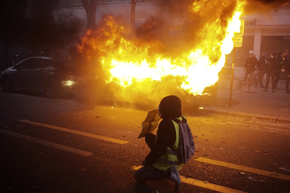 A protester kneels in front of a burning car during a demonstration, Saturday, Dec. 5, 2020 in Paris. Thousands marched in protests around France on Saturday against a contested security bill with tensions quickly rising at the Paris march as intruders set fire to several cars, broke windows and tossed projectiles at police. (AP Photo/Lewis Joly)