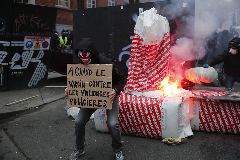 A protester holds a poster reading " When a vaccine against police violence" in front a barricade during a demonstration Saturday, Dec. 5, 2020 in Paris. Thousands marched in protests around France on Saturday against a contested security bill with tensions quickly rising at the Paris march as intruders set fire to several cars, broke windows and tossed projectiles at police. (AP Photo/Francois Mori)
