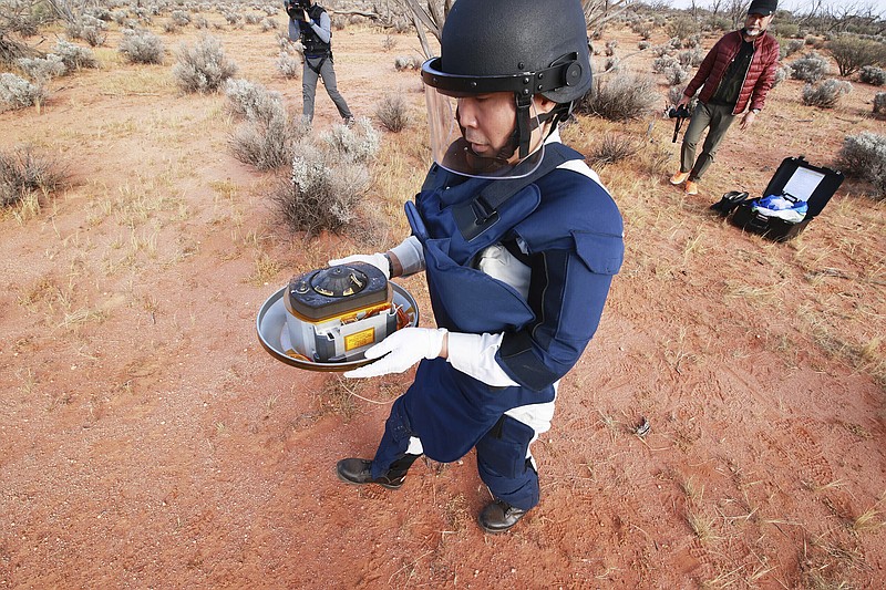 In this photo provided by the Japan Aerospace Exploration Agency (JAXA), a member of JAXA retrieves a capsule dropped by Hayabusa2 in Woomera, southern Australia, Sunday, Dec. 6, 2020. A Japanese capsule carrying the first samples of asteroid subsurface shot across the night atmosphere early Sunday before successfully landing in the remote Australian Outback, completing a mission to provide clues to the origin of the solar system and life on Earth. (JAXA via AP)