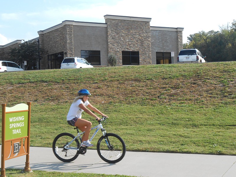 Courtesy of Xyta Lucas A bicyclist rides along the Wishing Springs trail below the buildings that have been built on the landfill between the south end of Lake Bella Vista and County Road 40.