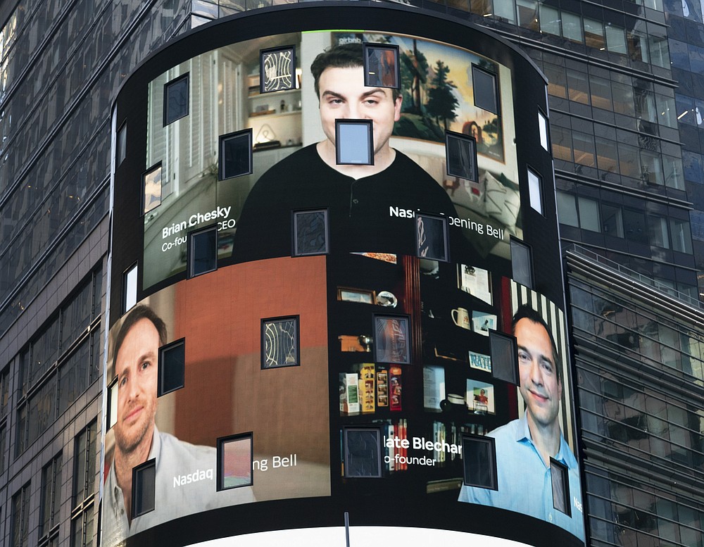 The electronic screen at the Nasdaq MarketPlace displays the Airbnb co-founders Brian Chesky, top, Joe Gebbia, left, and Nathan Blecharczyk, right, Thursday, Dec. 10, 2020, in New York. The San Francisco-based online vacation rental company holds its IPO Thursday. (AP Photo/Mark Lennihan)