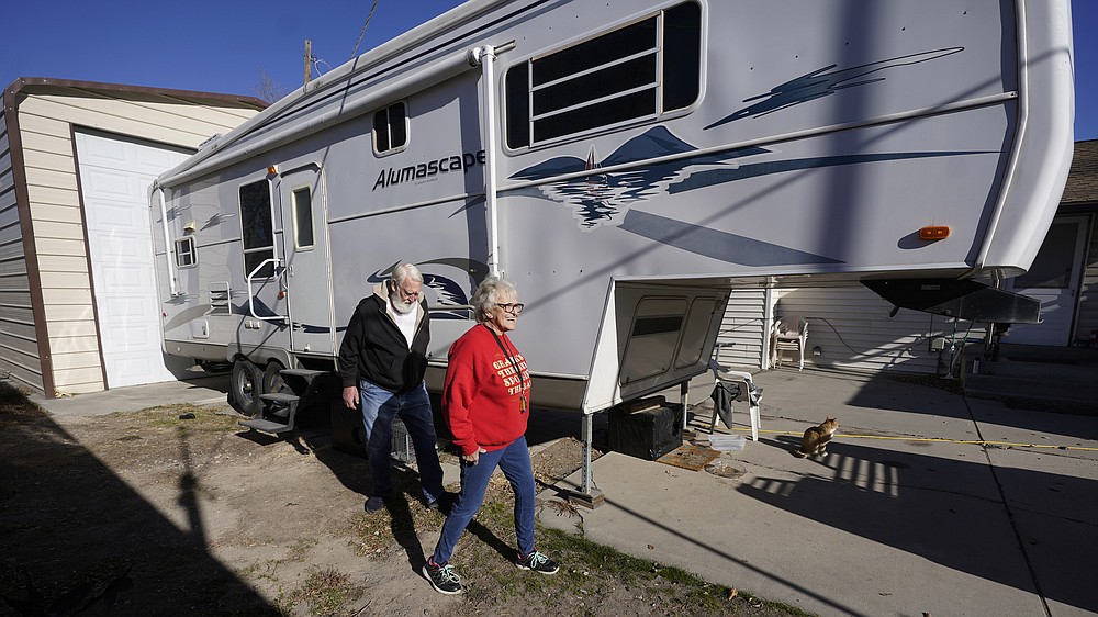 Kathy and Bud Scott walk past their fifth wheel travel trailer at their home Thursday, Dec. 3, 2020, in West Valley, Utah. Many snowbirds who live part time in warmer climates to escape cold weather won't be flocking south this winter. (AP Photo/Rick Bowmer)