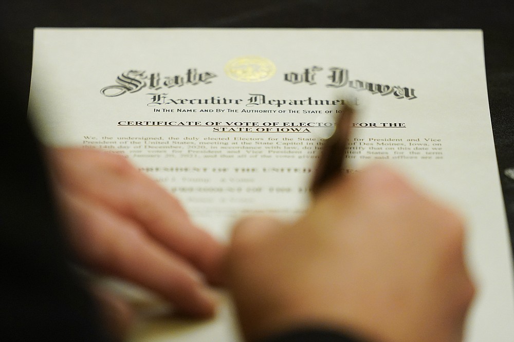 A member of Iowa's Electoral College signs the Certificate of Vote of Electors for the State of Iowa, Monday, Dec. 14, 2020, at the Statehouse in Des Moines, Iowa. (AP Photo/Charlie Neibergall)