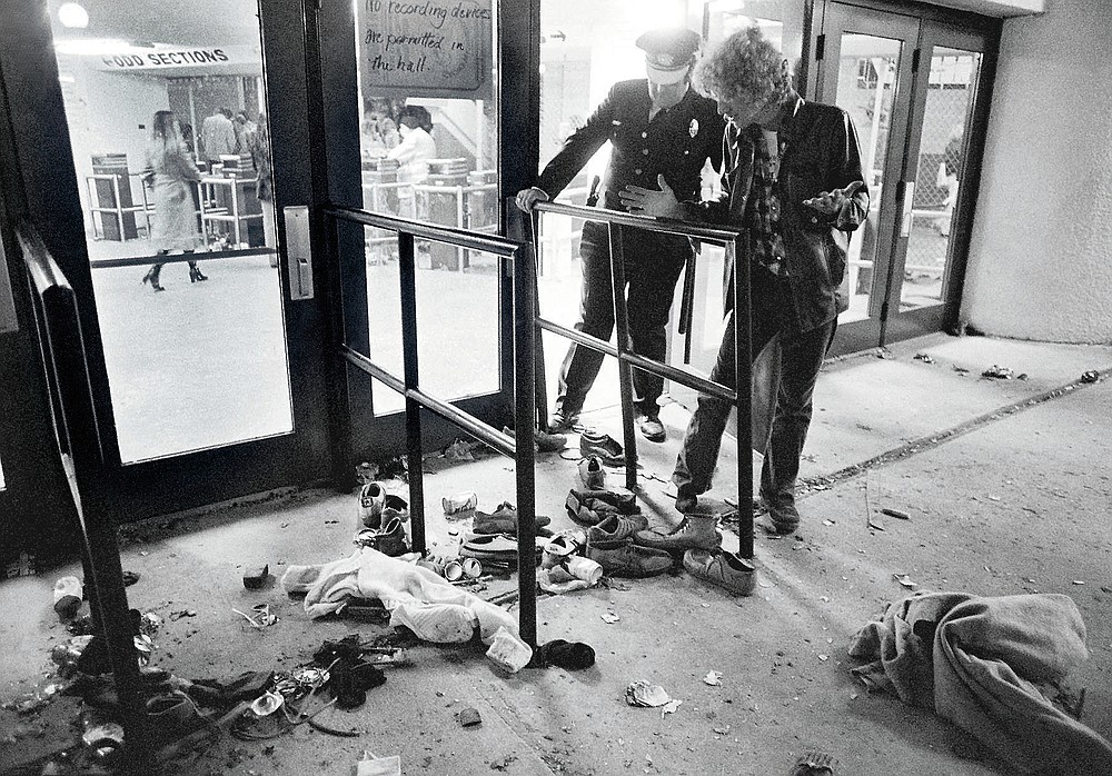FILE - In this Dec. 3, 1979, file photo, a security guard and an unidentified man look at an area where several people were killed as they were caught in a surging crowd entering Cincinnati's Riverfront Coliseum for a concert by the British rock band The Who. Alumni of nearby Finneytown High School, who lost three classmates in the tragedy, faced obstacles in 2020 to their annual memorial scholarship fund-raising event. In the end, they created a show of prerecorded video interviews with The Who's frontman, Roger Daltrey, guitarist-songwriter Pete Townshend and a mix of recorded and live discussions with relatives of the 11 people killed in the tragedy. (AP Photo/Brian Horton, File)