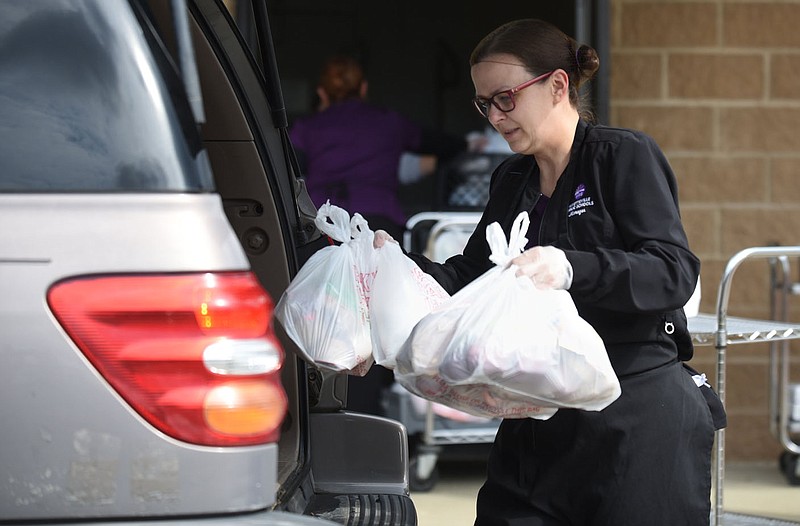 Shonda Holt, kitchen manager at Happy Hollow Elementary School, places bags of meals March 31 in cars at Owl Creek School in Fayetteville. Go to nwaonline.com/201220Daily/ and nwadg.com/photos for a photo gallery.
(File Photo/NWA Democrat-Gazette/David Gottschalk)