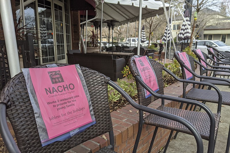 This Monday, Dec. 21, 2020, photo shows a line of empty chairs bearing the names of workers who have lost their jobs during the pandemic, outside Crumbs restaurant in Danville, Calif. (AP Photo/Michael Liedtke)