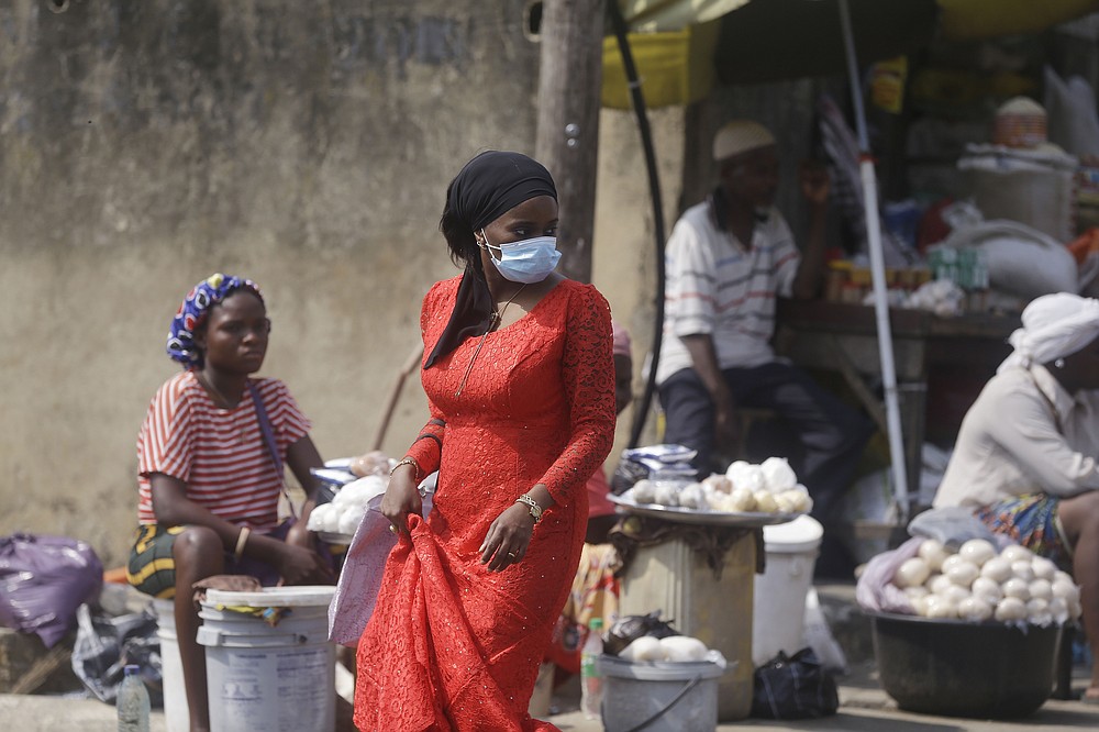 A woman wearing a face mask to protect against coronavirus, walks past people selling food at a market in Lagos, Nigeria, Thursday Dec. 24, 2020. Africa’s top public health official says another new variant of the coronavirus appears to have emerged in Nigeria, but further investigation is needed. The discovery could add to new alarm in the pandemic after similar variants were announced in recent days in Britain and South Africa and sparked the swift return of travel restrictions. (AP Photo/Sunday Alamba)