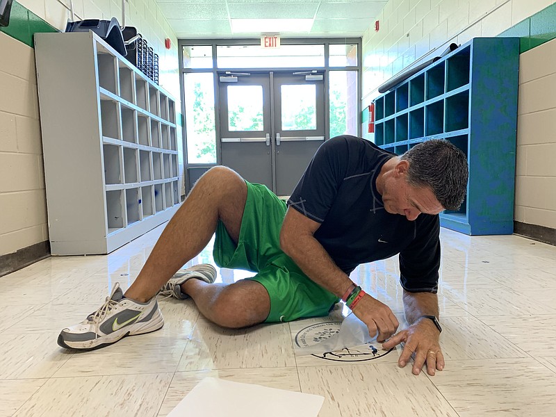 Alan Barton, longtime Greenland Elementary School principal, applies decals to the floor to help students with social distancing Thursday, Aug. 6, 2020, as he and his staff prepare the school to meet social-distancing and other covid-19 standards ahead of the first day of school.
(NWA Democrat-Gazette/Andy Shupe) story.lead_photo.caption