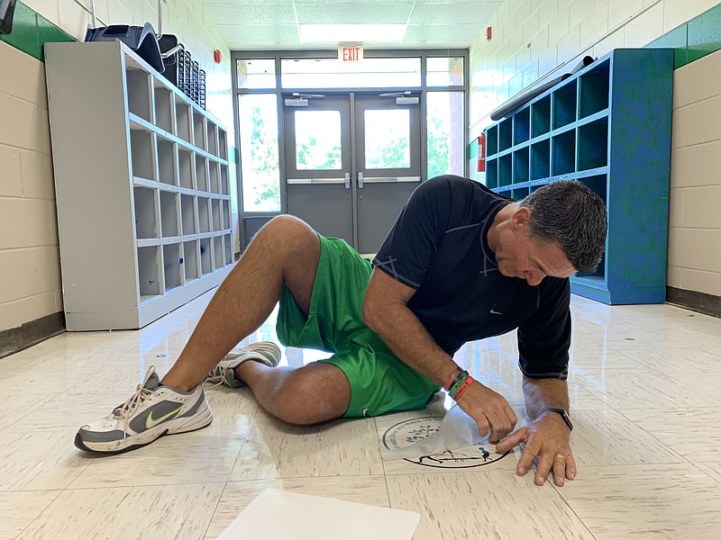 Alan Barton, longtime Greenland Elementary School principal, applies decals to the floor to help students with social distancing Thursday, Aug. 6, 2020, as he and his staff prepare the school to meet social-distancing and other covid-19 standards ahead of the first day of school. 
(NWA Democrat-Gazette/Andy Shupe)