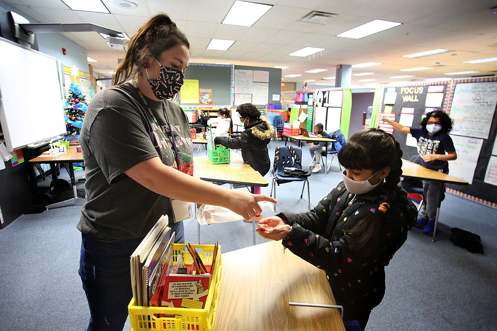 Sarah McPherson, Dodd Elementary third-grade teacher at Dodd Elementary School, gives a squirt of hand sanitizer Dec. 11 to student Sahory Lara after wiping down her desk at the school in Little Rock. 
Check out nwaonline.com/201228Daily/ and nwadg.com/photos for a photo gallery.
(Arkansas Democrat-Gazette/Thomas Metthe)