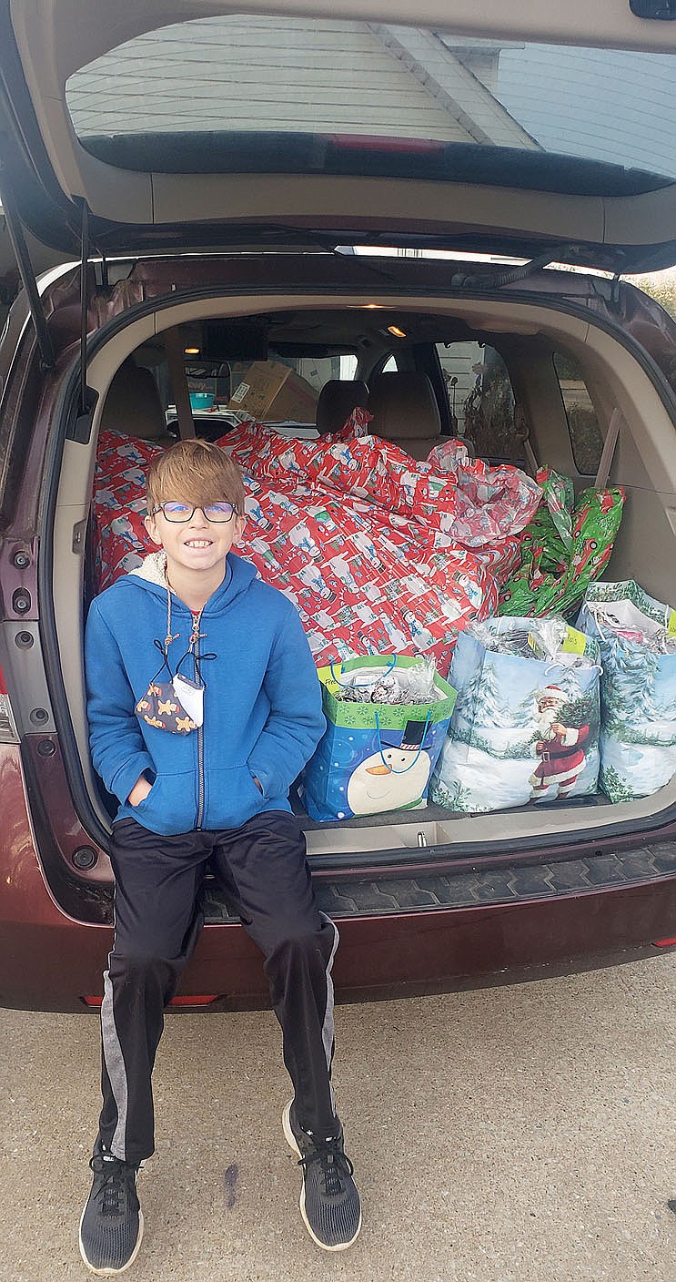 COURTESY PHOTO Jaxton Jowers of Farmington sits in front of Christmas presents he is delivering to the residents at Peachtree Village in Farmington. Jaxton raised money for the gifts by making "Mask Keepers," a strap made of parachute cord with clips tied to each end. People can then attach their facemasks to each clip so the mask will hang around the neck when it's not being worn.