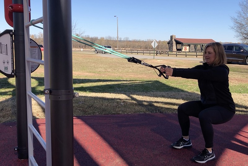 Hannah Pinkston demonstrates step 2 of the Stretch Band Pulsing Squat using a ladder in the AARP FitLot at Little Rock's Murray Park. (Arkansas Democrat-Gazette/Celia Storey)