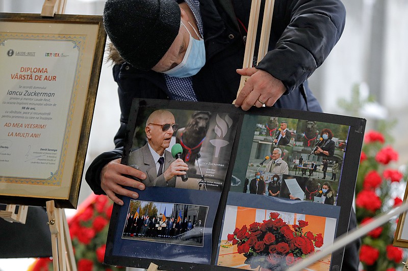 A man adjusts images of Iancu Tucarman, during his funeral, at a Jewish cemetery in Bucharest, Romania, Monday, Jan. 11, 2021. Tucarman, one of the last remaining Holocaust survivors in Romania, on was buried after dying from COVID-19 last week at the age of 98. (AP Photo/Vadim Ghirda)