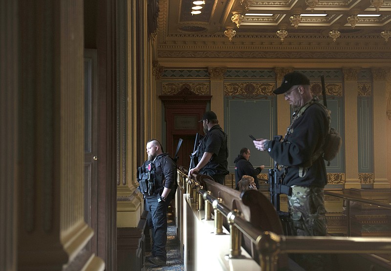 FILE - In this April 30, 2020, file photo, armed members of a militia group watch the protest outside while waiting for the Michigan Senate to vote at the Capitol in Lansing, Mich. Michigan has banned the open carry of guns in the state Capitol a week after an armed mob rioted in the U.S. Capitol and following an attempt to storm the statehouse last year. (Nicole Hester/MLive.com/Ann Arbor News via AP File)
