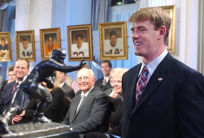 FILE - USC quarterback Carson Palmer, right, smiles at the Heisman Trophy after being named the 2002 Heisman Trophy winner at The Yale Club in New York, in this Dec. 14, 2002, file photo. Heisman Trophy winner Carson Palmer and former Oklahoma coach Bob Stoops are among the 13 former players and coaches who make up the latest College Football Hall of Fame class.  The National Football Foundation announced the newly elected hall of famers Monday, Jan. 11, 2021. This class will be inducted in December. (AP Photo/Suzanne Plunkett, File)